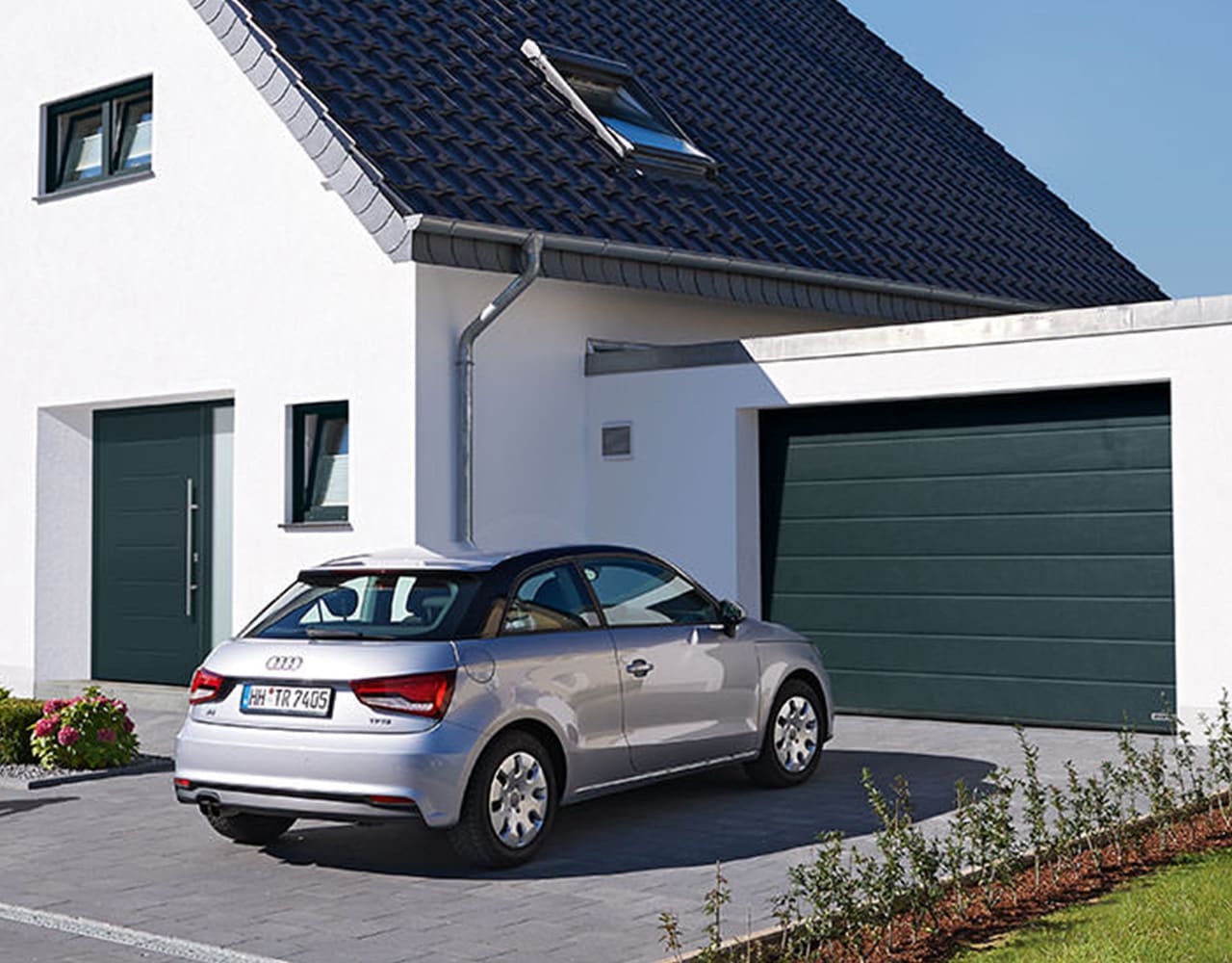 Garagentore und Haustüren eingebaut in einem Einfamilienhaus mit Auto vor der Garage.